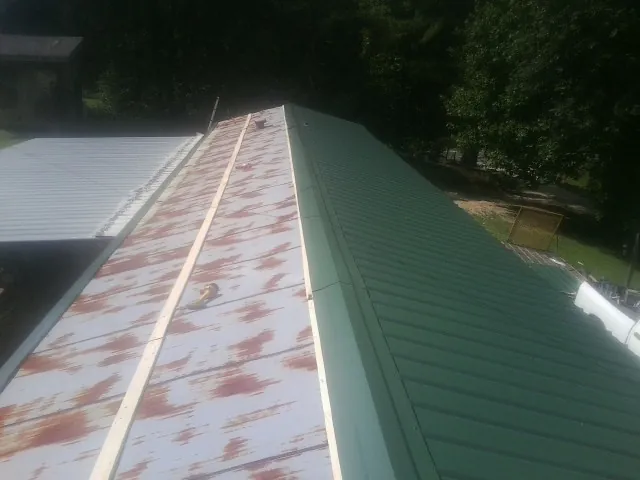 Old rusted panels beside newly installed green metal roofing — Wind Damage Roof Repair by Roofing Brothers in Big Run