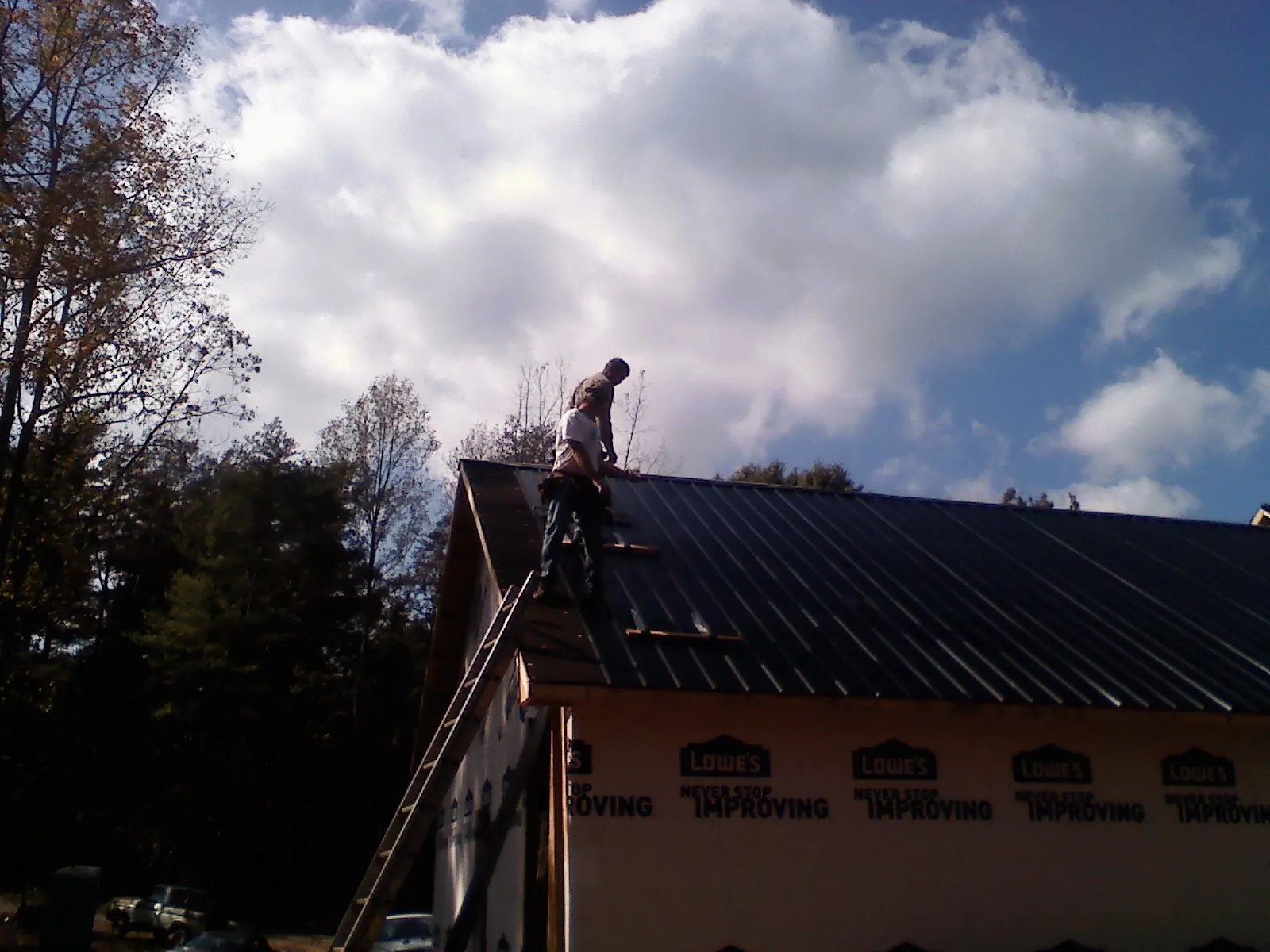 Roofer fastening dark metal panels high against a cloudy sky, from a Roof Inspection job in Big Run