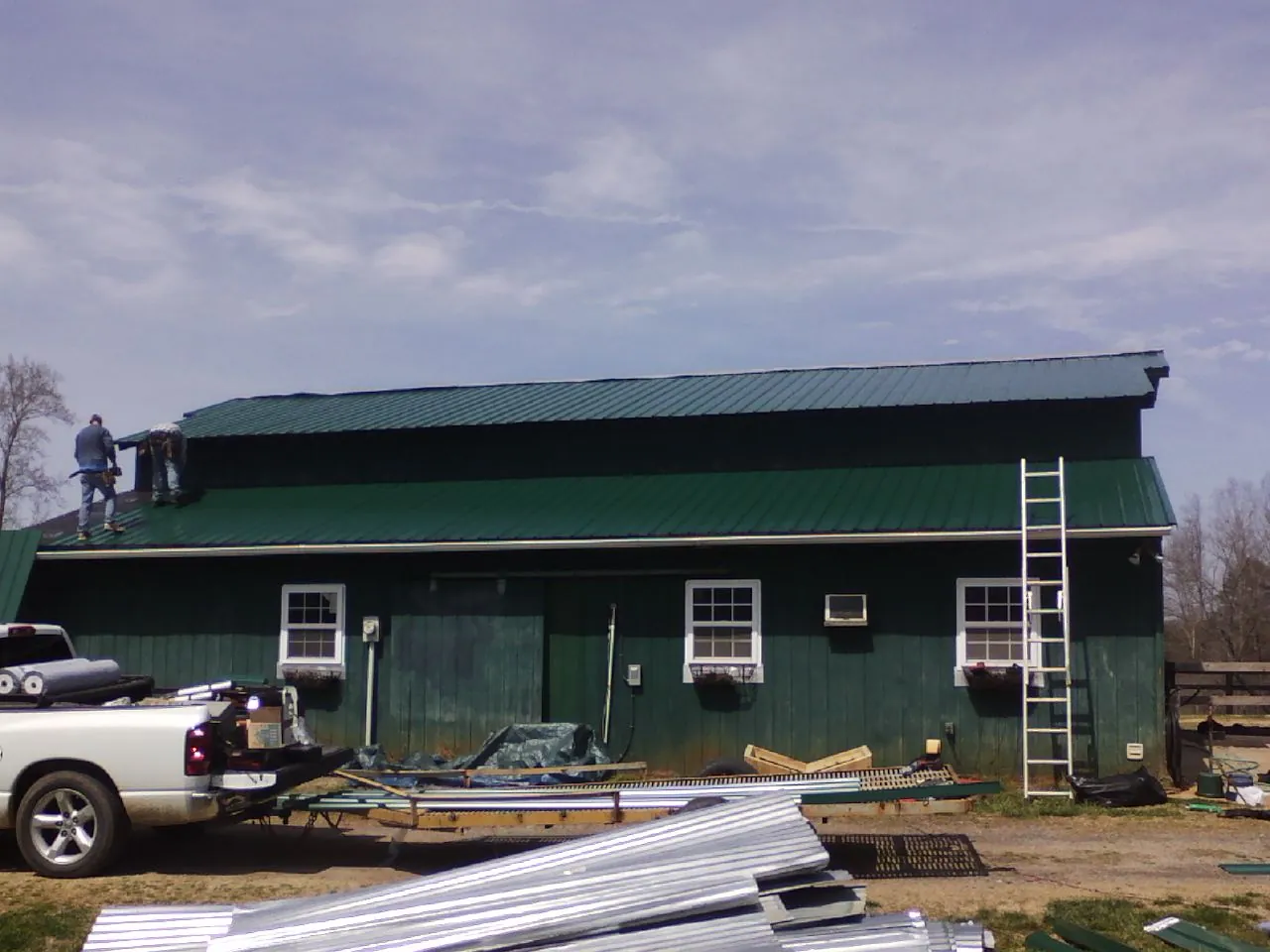 Crew installing green metal roofing on a large green barn in Big Run