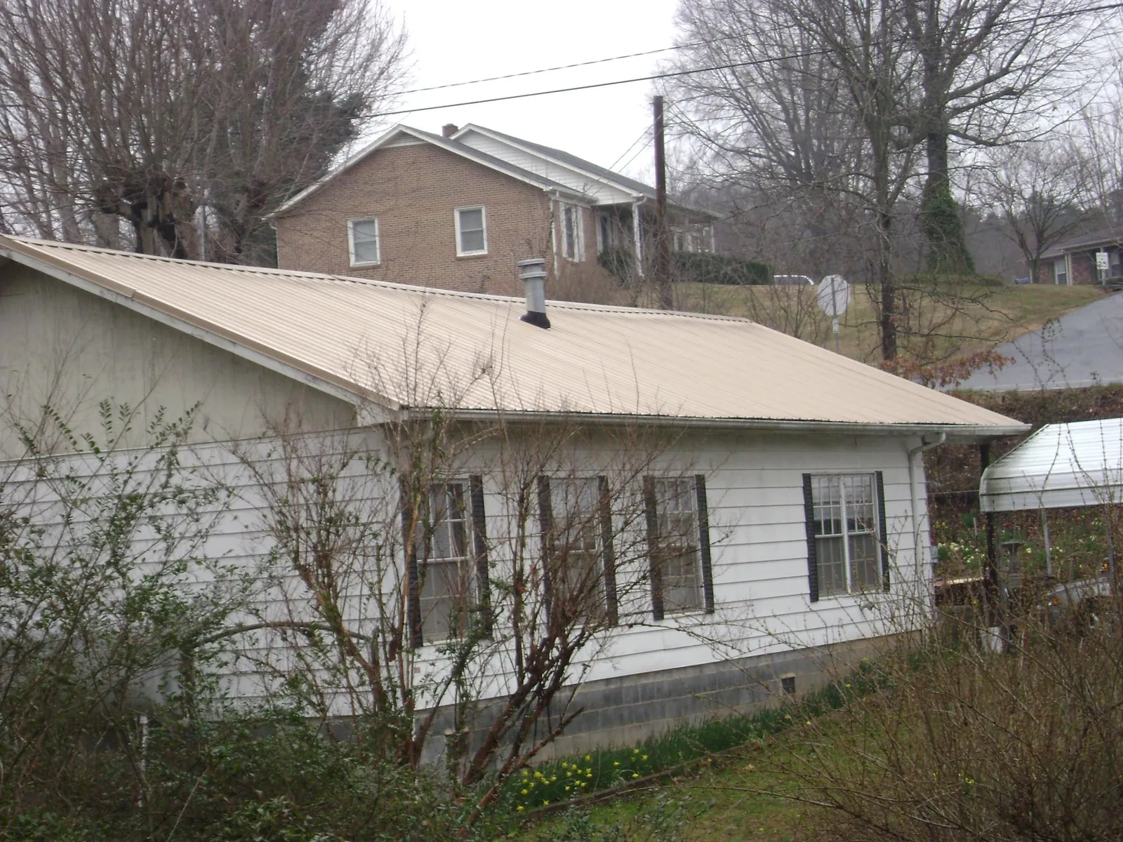 Tan metal roof on a white sided house set into a hillside — Commercial Roofing by Roofing Brothers in Big Run